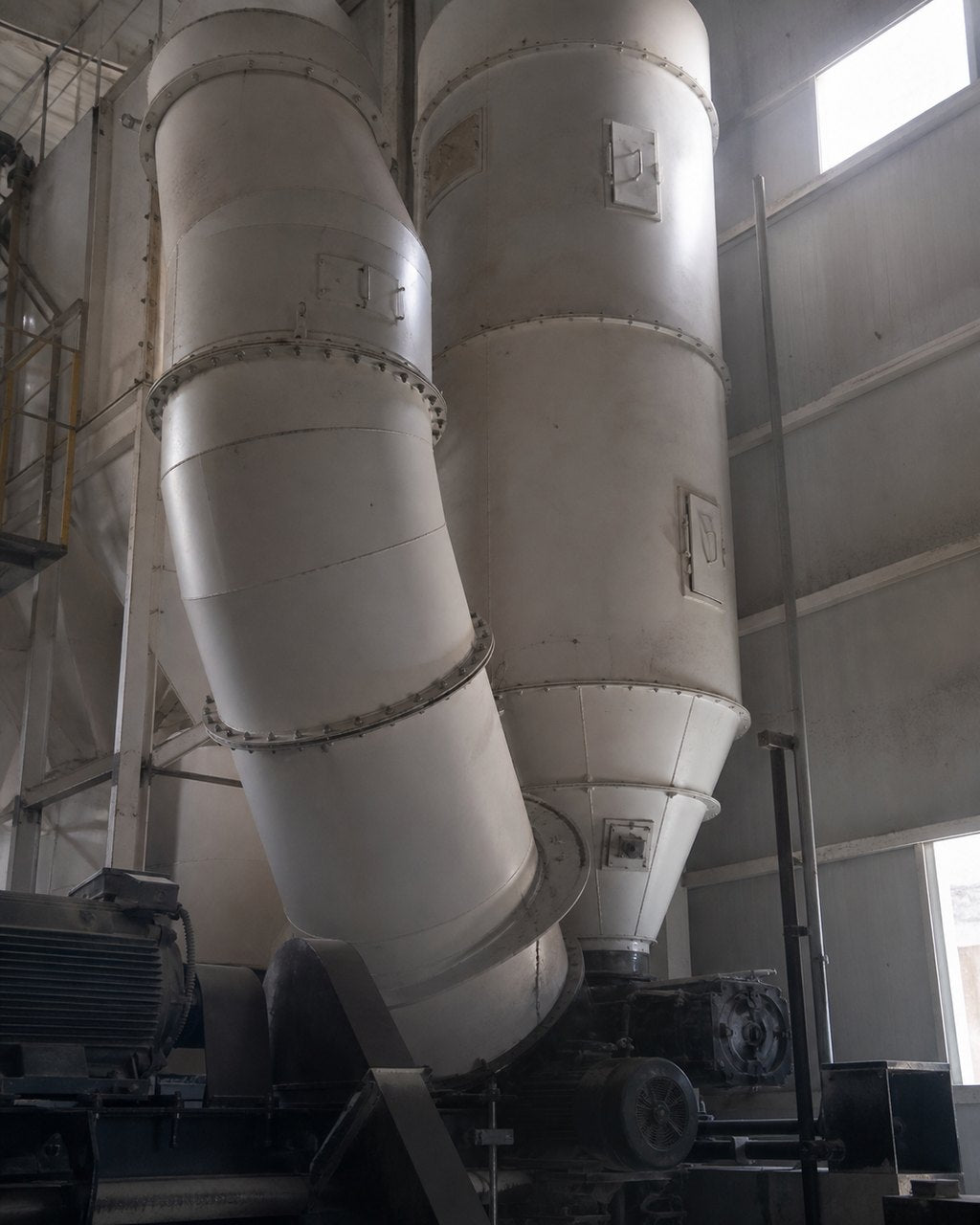 Large steel cyclones and ducting in a kernel plant, the pale conical vessels rising into the roof space of the shed.