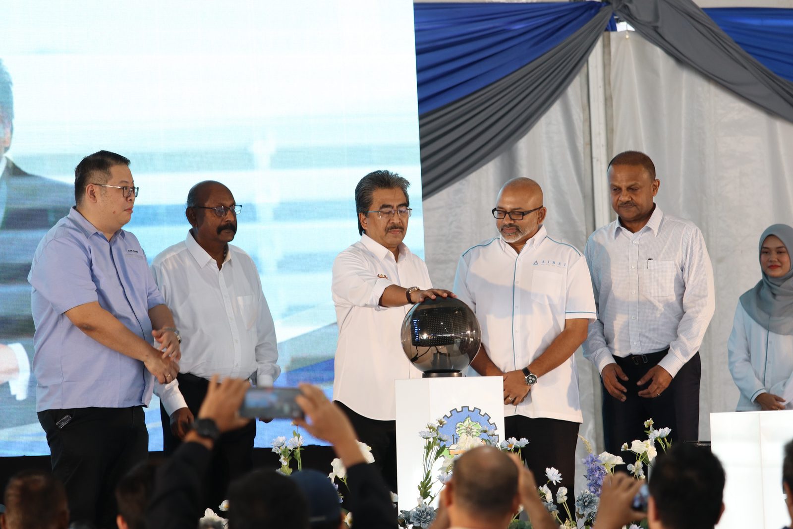 The launch ceremony on stage: a group of officials and AIREI staff around a covered globe, photographers in the foreground.