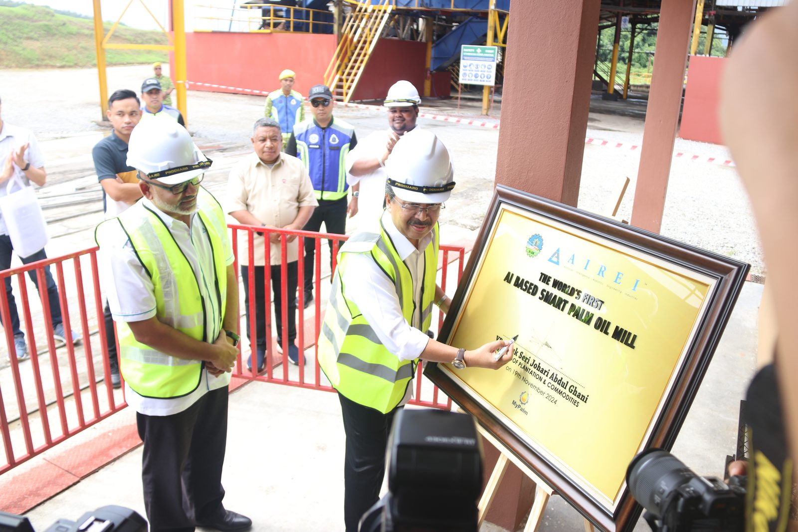 The commemorative plaque for the world’s first AI-based smart palm oil mill being unveiled by two men in hard hats and hi-vis vests at the mill.