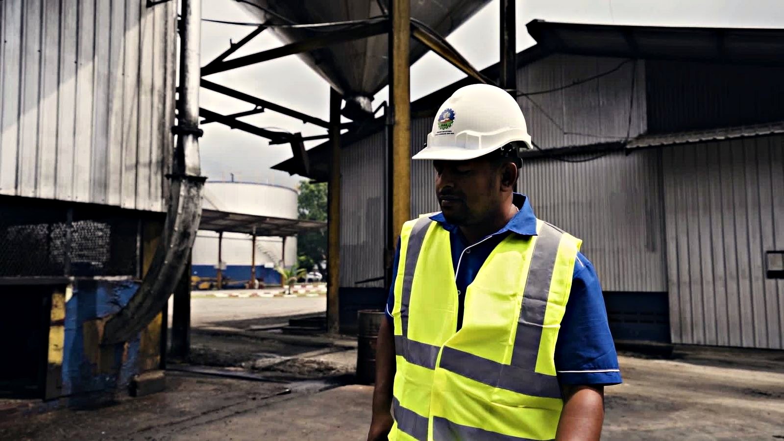 An engineer in a hard hat and hi-vis vest walking the mill yard between the process house and the storage tanks.